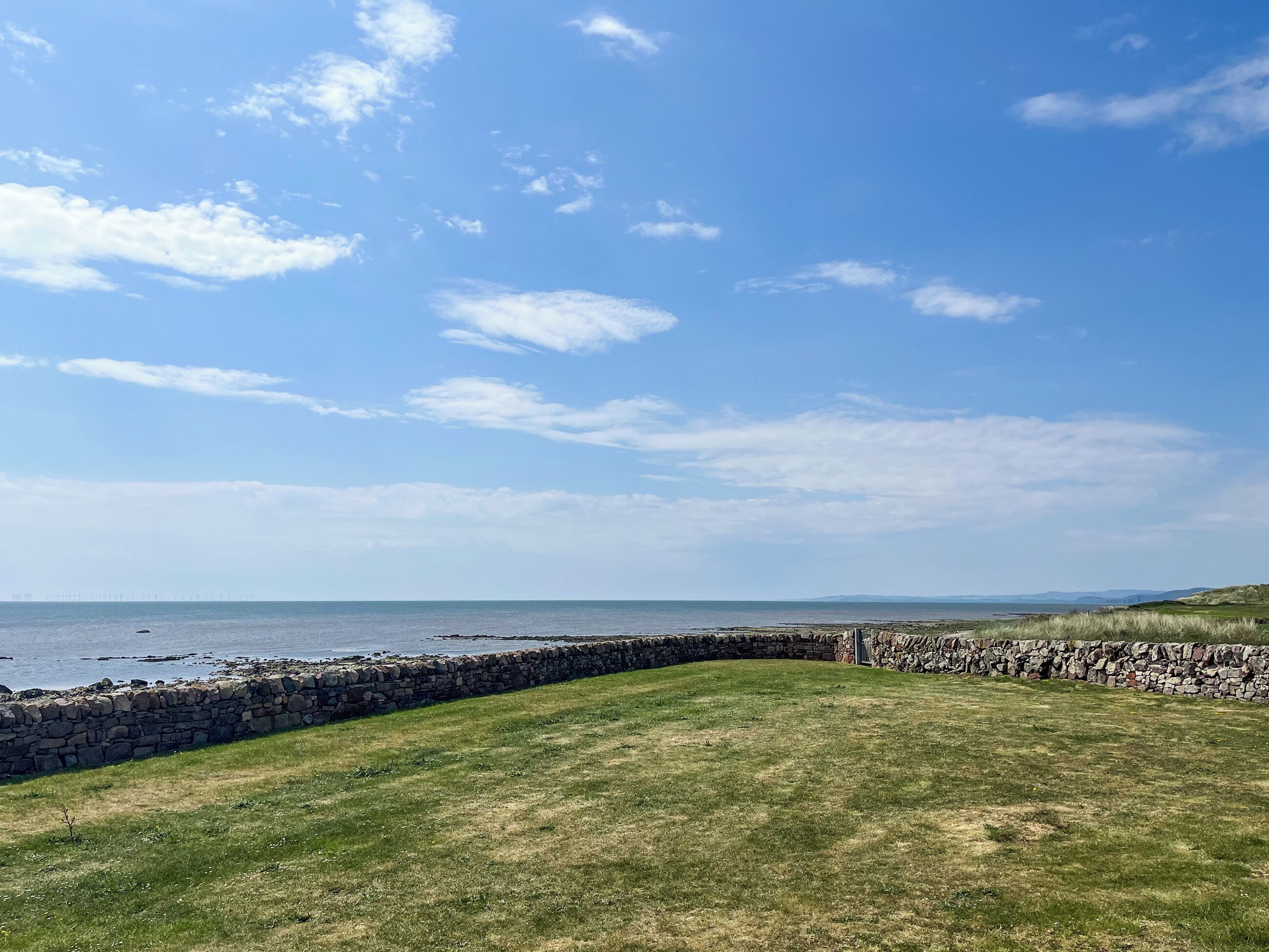 Ein grasbewachsenes Feld mit einer Steinmauer und Blick auf das Meer.