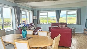 Um quarto espaçoso com mesa de jantar de madeira, sofá de couro vermelho e grandes janelas com vista para o campo.