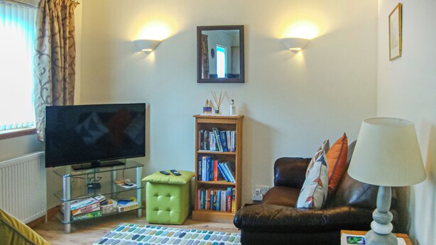Una sala de estar con televisor, estantería, sofá, mesa de centro y lámpara.