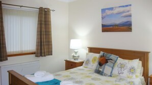 Una cama bien hecha con un edredón estampado con motivos florales, una lámpara de noche y un cuadro en la pared.