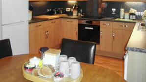 Una cocina con armarios de madera, un refrigerador, un lavavajillas y una mesa de comedor con una bandeja de alimentos para el desayuno.