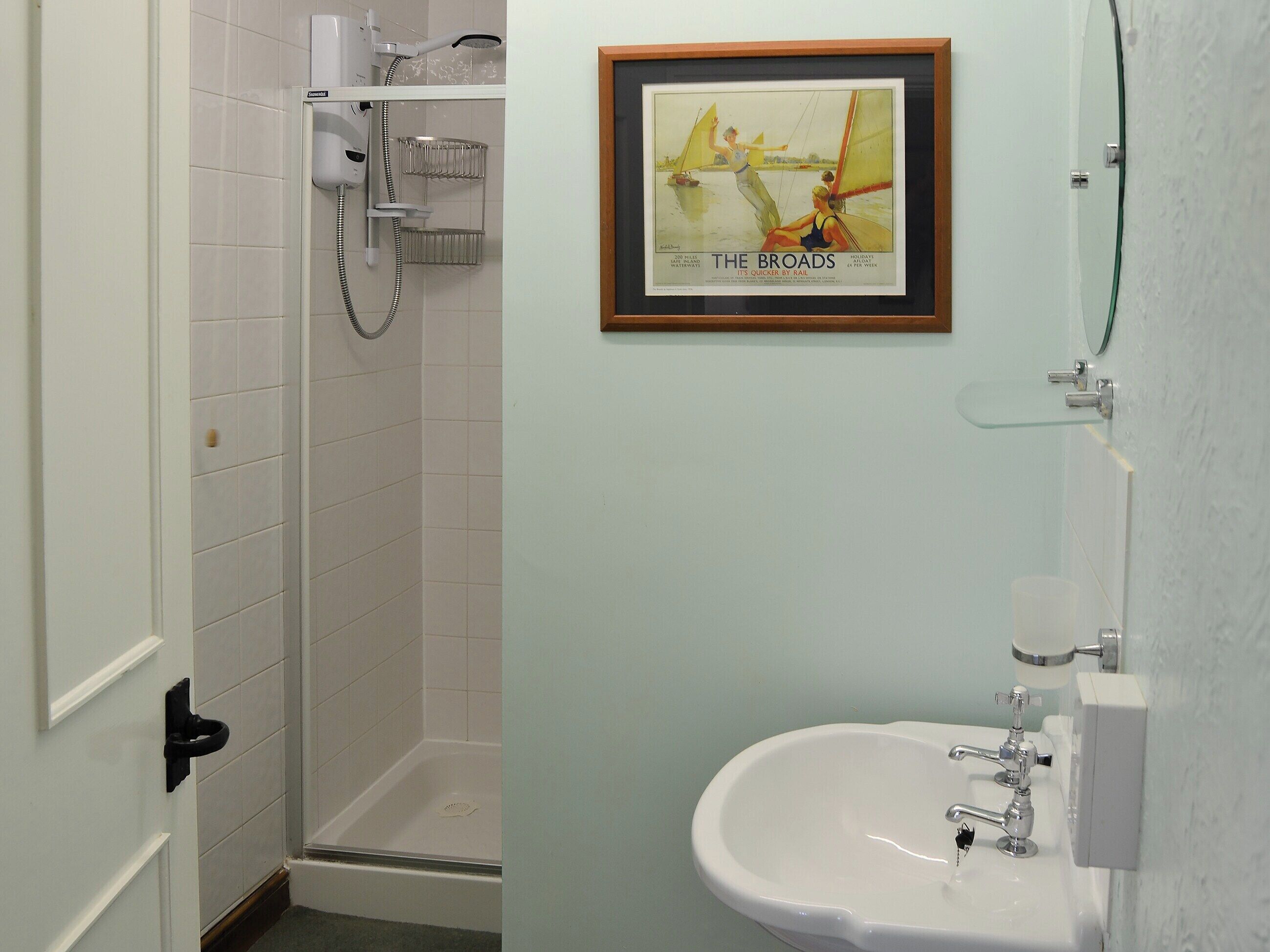 Une salle de bain avec une douche, un lavabo et une affiche encadrée au mur.