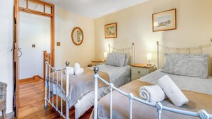Habitación de hotel con dos camas, suelo de madera, puerta con marco de madera y una lámpara en el techo.