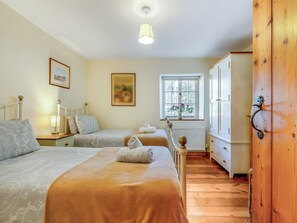 Quarto com duas camas, janela florida, guarda-roupa de madeira e radiador.