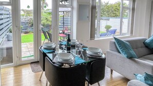 Uma área de refeições com uma mesa posta para quatro pessoas, cadeiras e um sofá com almofadas.