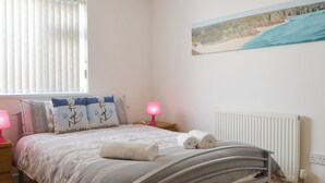 Quarto com cama, almofadas, um quadro, mesa de cabeceira, luminária e radiador.