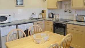A compact kitchen with a microwave, sink, stove, and dishwasher. There are wooden chairs around a small table. - 3 bedroom accommodation in Whitby (Whitby)