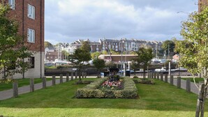 A well-maintained garden with a central flower bed, surrounded by a brick building and a row of houses in the background. - 3 bedroom accommodation in Whitby (Whitby)