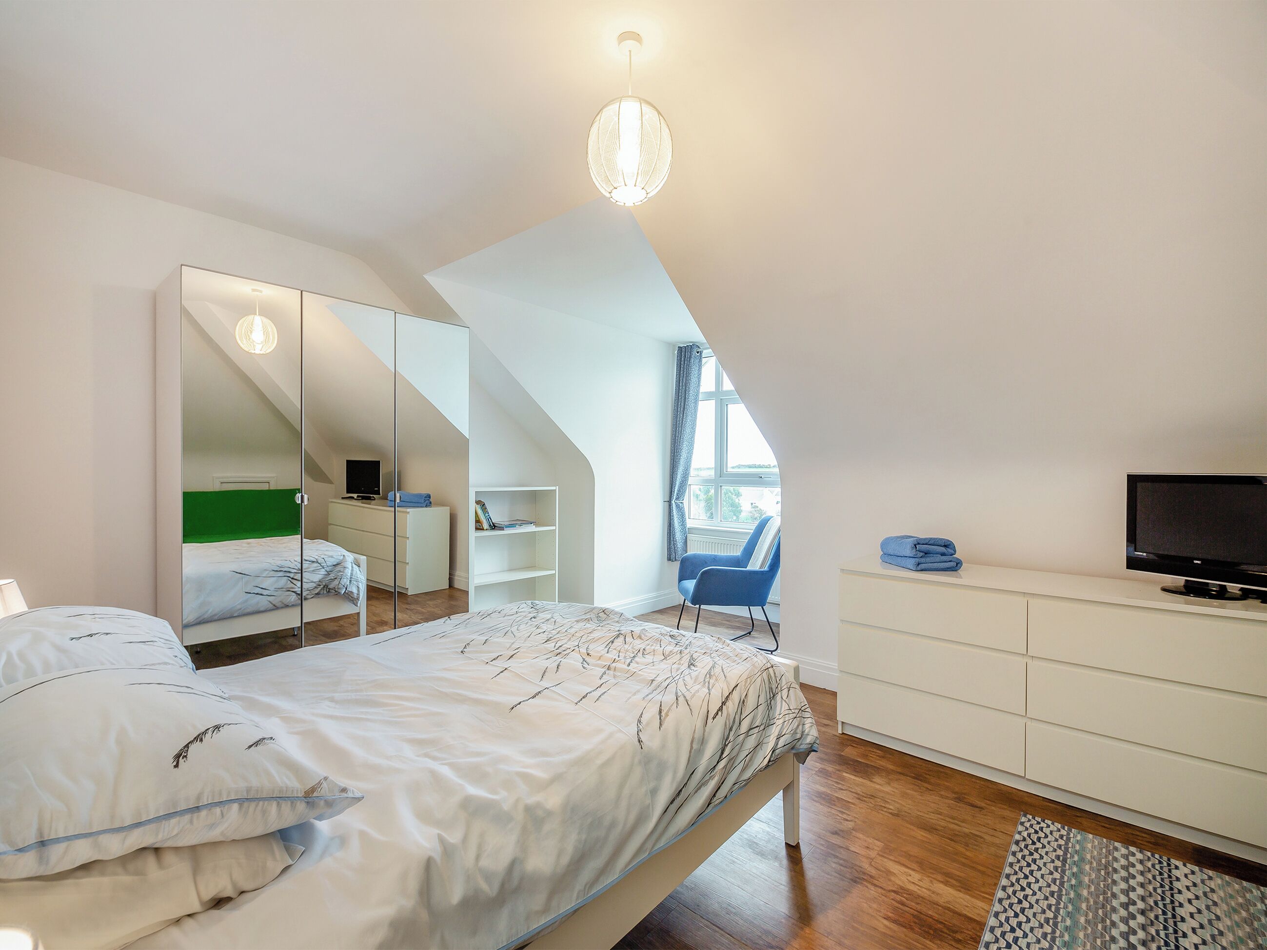 A bedroom with a bed, a dresser, a TV, and a chair.
