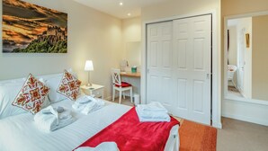 A hotel room with a bed, a desk, a chair, a wardrobe, and a painting on the wall. - Barn Owl Cottage - 27941 (Stirling)