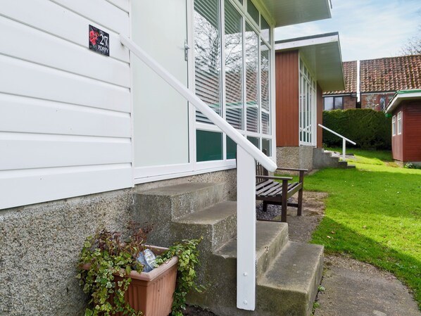 A residential building with a white exterior, a visible number '27', and a small garden area with a wooden bench and a planter with greenery. - 2 bedroom accommodation in Cromer (Cromer)