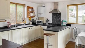 Une cuisine moderne avec des meubles blancs, un plan de travail noir, une hotte en acier inoxydable et une fenêtre équipée de stores.