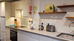 Eine moderne Küche mit weißen Schränken, einem eingebauten Backofen, einer Kaffeemaschine, einem Toaster und einem Vintage-Radio auf einem Holzregal.