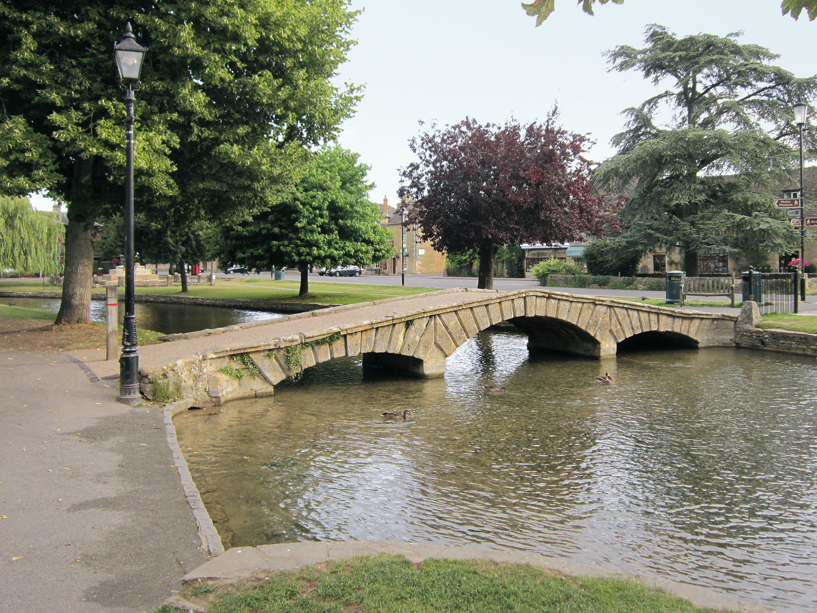 Un pont de pierre enjambant une étendue d’eau paisible, entouré d’arbres et bordé d’un sentier.