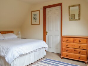 Une chambre à coucher avec un lit, une commode en bois, une porte et un tableau encadré au mur.