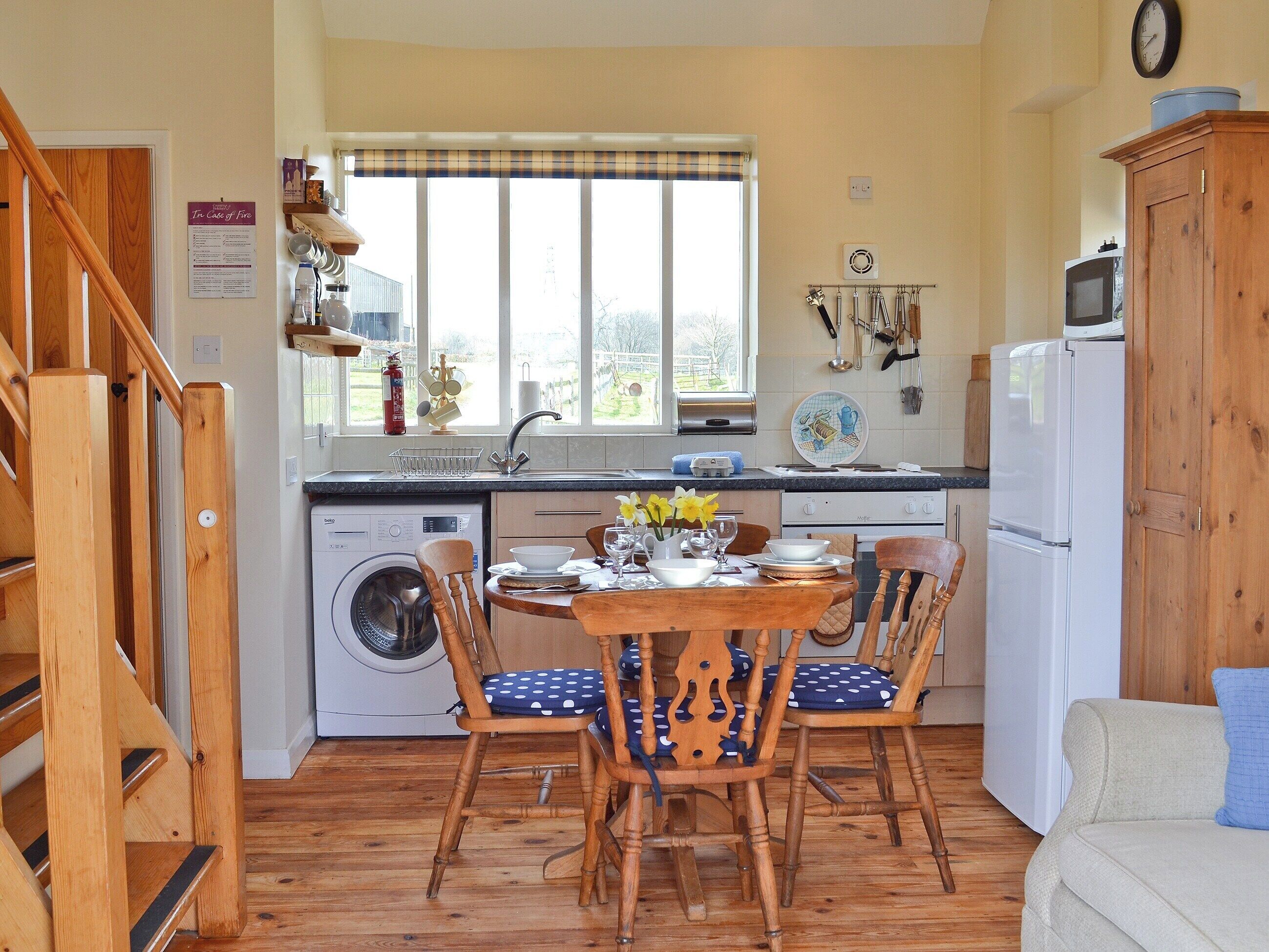 A kitchen with wooden flooring, a dining table with chairs, a washing machine, and a refrigerator.