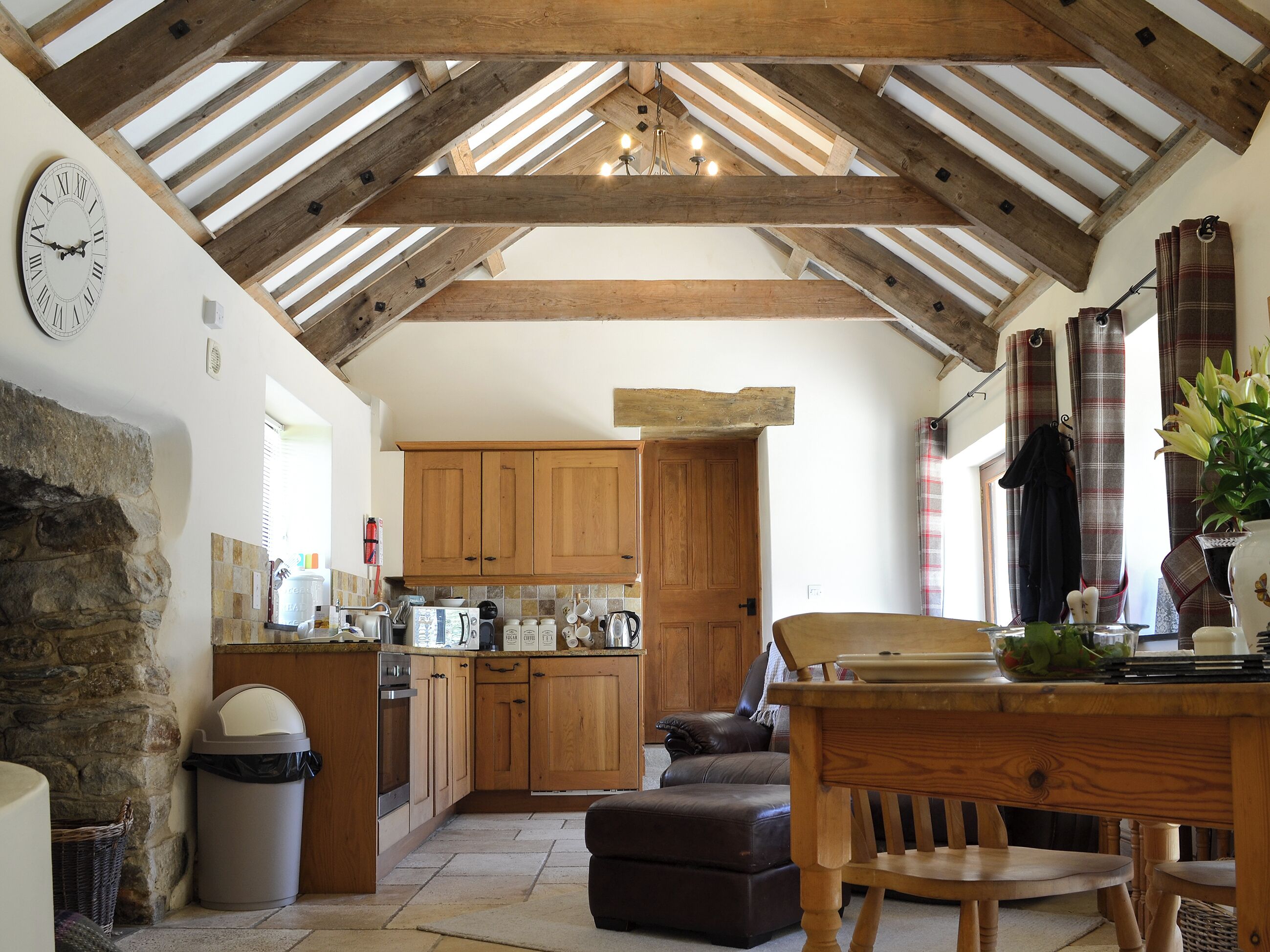 A rustic kitchen with wooden beams, a stone wall, and a clock.