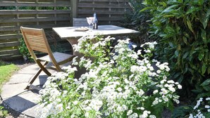 A patio with a table and chair, surrounded by lush greenery and white flowers. - 1 bedroom accommodation in Mevagissey (Mevagissey)