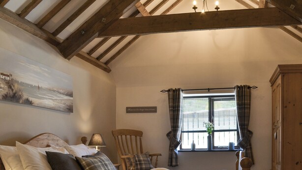 A bedroom with a bed, a chair, a window with curtains, a lamp, and a painting on the wall. - 1 bedroom accommodation in Mevagissey (Mevagissey)