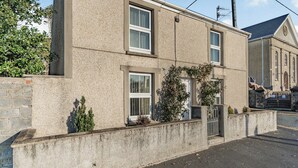 A two-story building with a stone facade, multiple windows, and a small garden area with plants and a tree. - 2 bedroom accommodation in Pembrey, near Burry Port (Pembrey, near Burry Port)