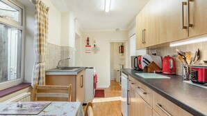 A compact kitchen with a sink, stove, and refrigerator. There is a dining table with chairs and a window with curtains. - 2 bedroom accommodation in Pembrey, near Burry Port (Pembrey, near Burry Port)