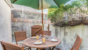 A round wooden table with four chairs, a green umbrella, and a brick wall in the background. - 2 bedroom accommodation in Pembrey, near Burry Port (Pembrey, near Burry Port)