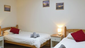 Et hotelværelse med to enkeltsenge, begge med trægavl, hvidt sengetøj og røde puder. Der er to sengeborde med lamper, og værelset har et enkelt, rent design.