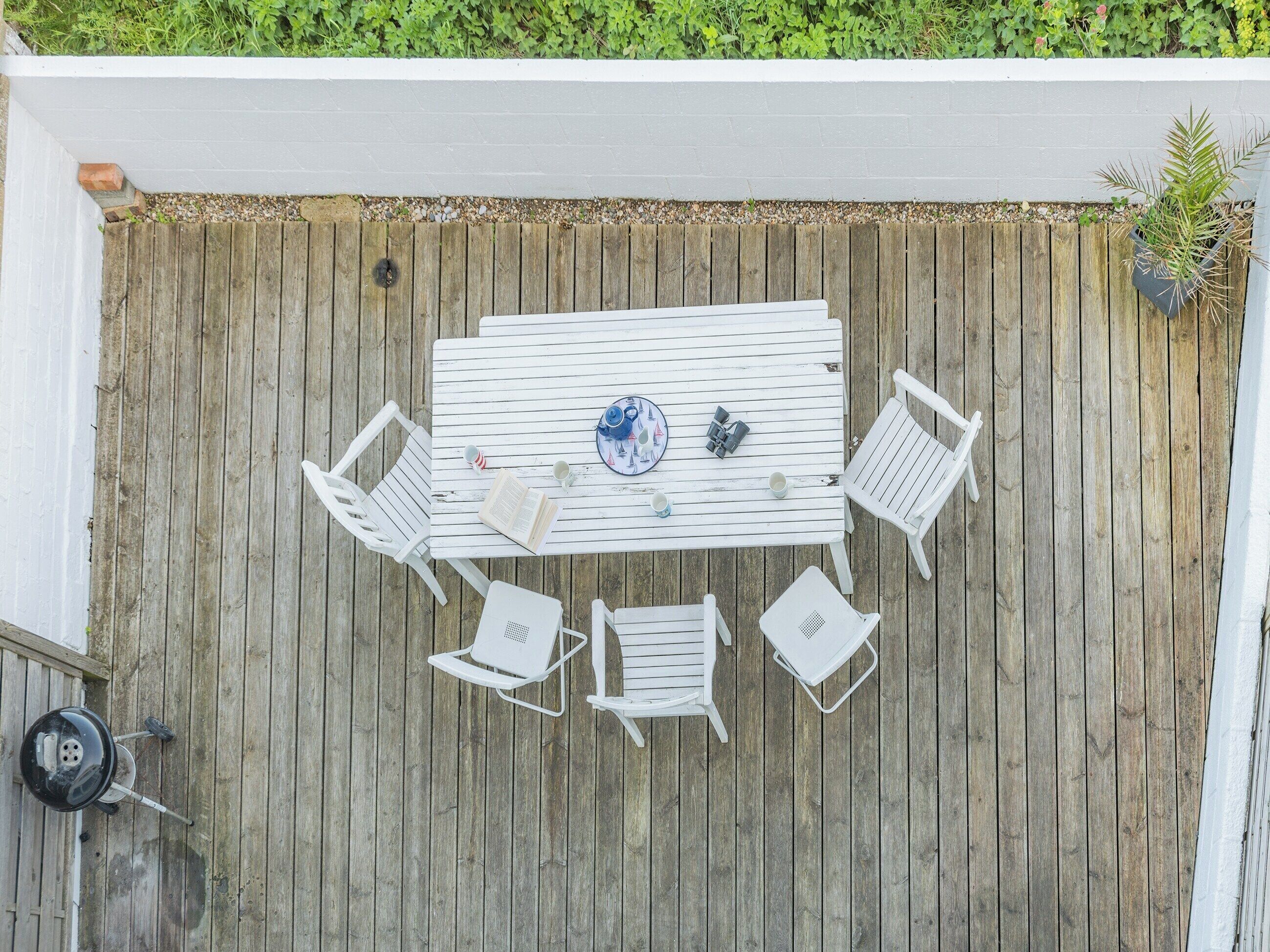 A wooden deck with a white table and chairs, a small potted plant, and a security camera.
