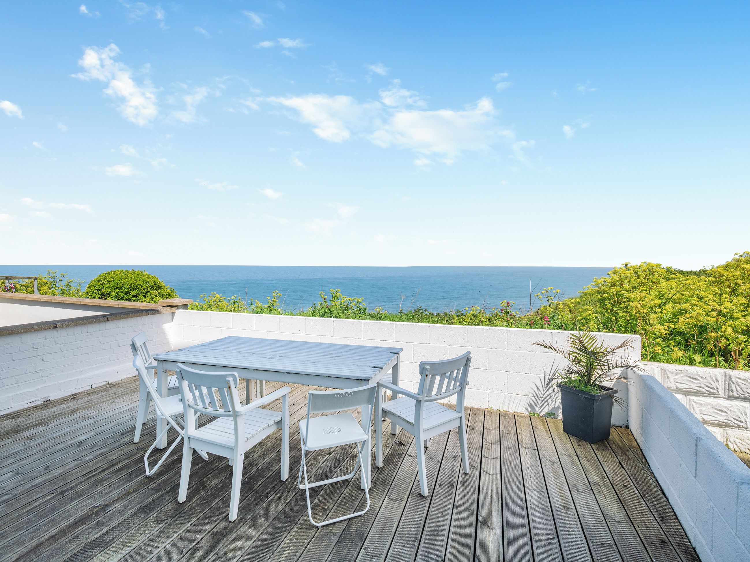 A wooden deck with a table and chairs, overlooking a body of water.