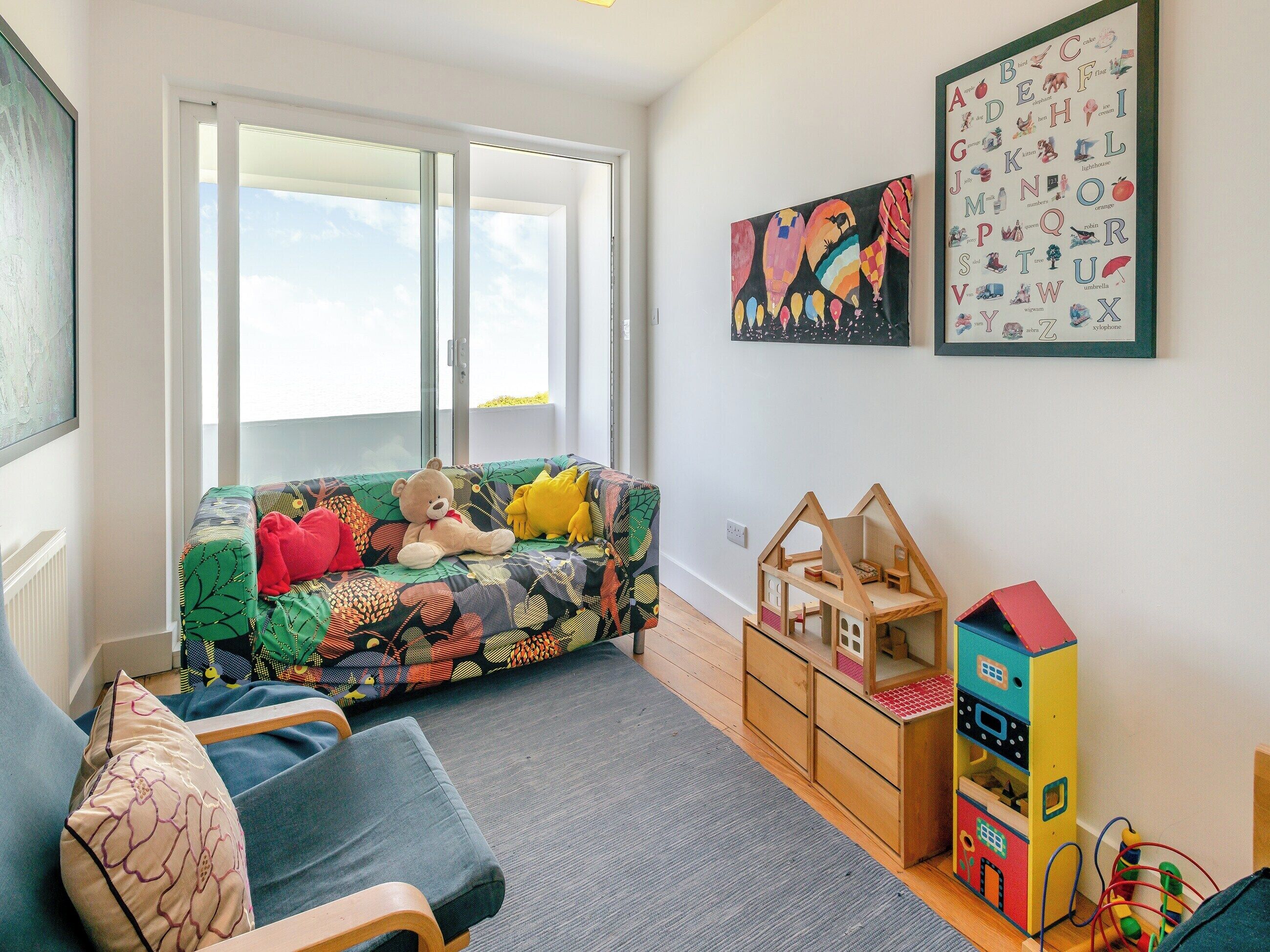 Een gezellige woonkamer met een kleurrijke bank, een houten poppenhuis en wanddecoratie met letters.