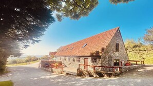 A stone building with a sloped roof, a fenced driveway, and a view of the surrounding landscape. - Cider House is a paradise for families, friends and couples. (Hawkchurch, near Lyme Regis)