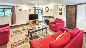 A living room with red sofas, a wooden coffee table, a flat-screen TV, and a fireplace. - Cider House is a paradise for families, friends and couples. (Hawkchurch, near Lyme Regis)
