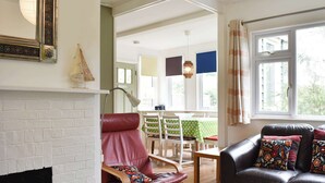 Een woonkamer met een open haard, een leren bank, een schommelstoel en een eethoek met een tafel en stoelen.