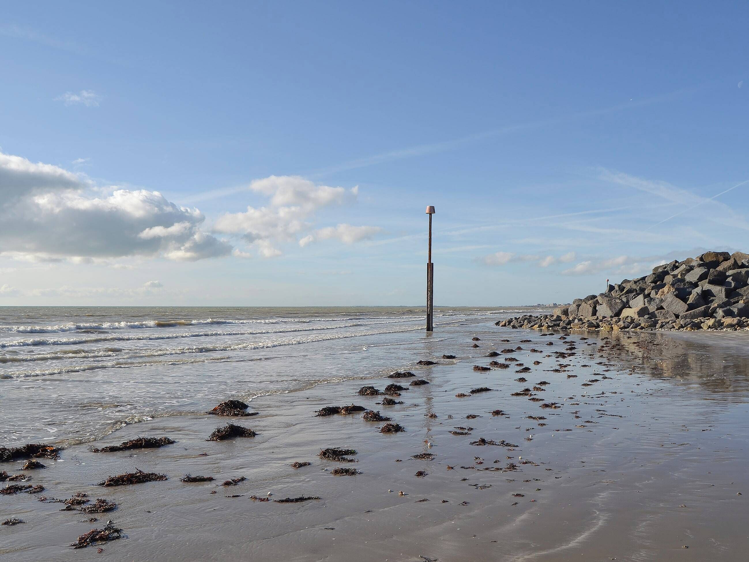 Une plage avec un rivage rocheux, des vagues et un grand poteau visible au loin.