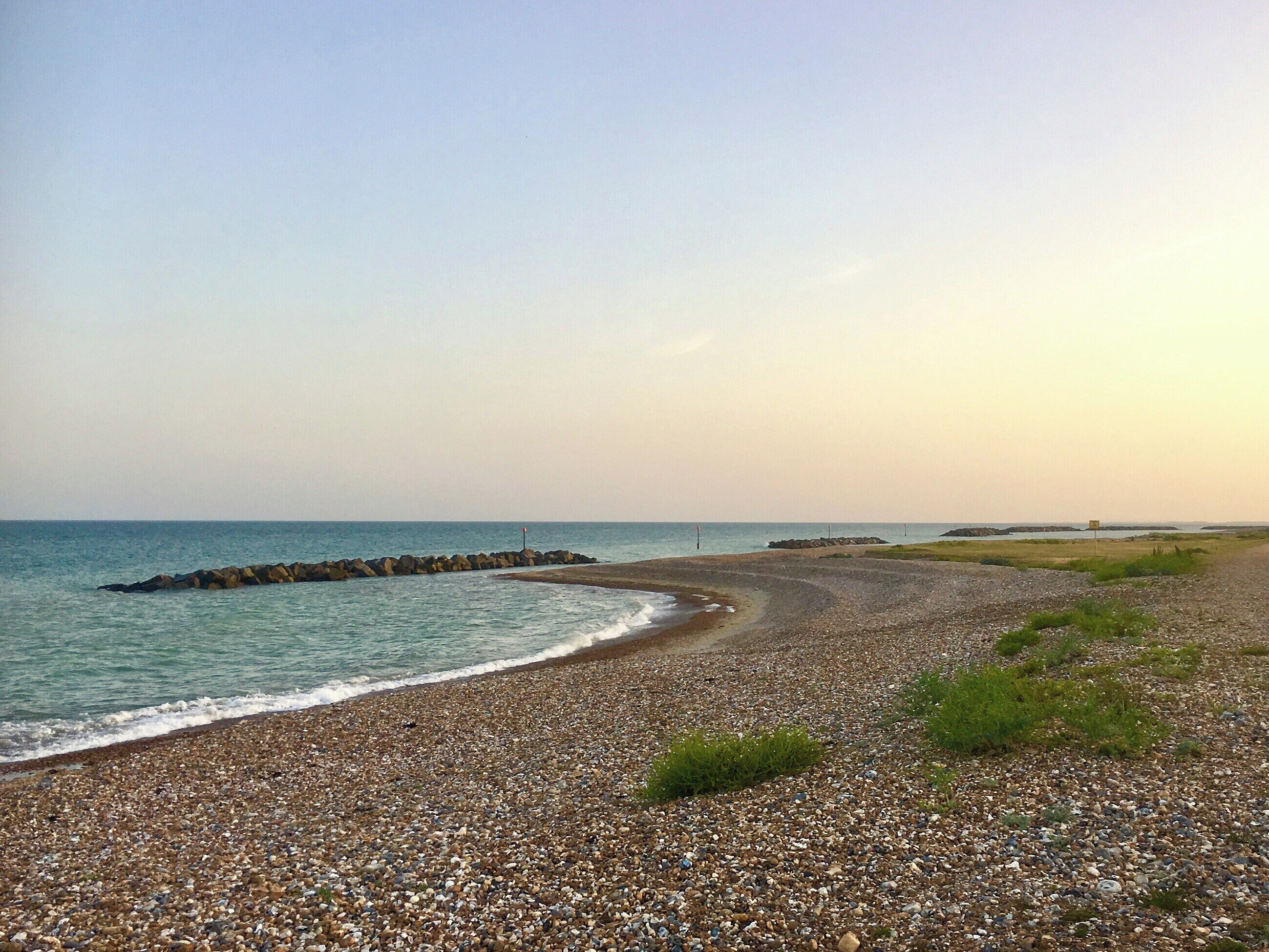 Une plage de galets, avec une digue rocheuse et une mer calme.