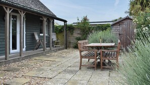 Een terras met een houten tafel en stoelen, een overdekte zithoek en een tuin met verschillende planten.