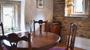 Un coin repas rustique avec une table et des chaises en bois, un vase rempli de fleurs et un mur en pierre.