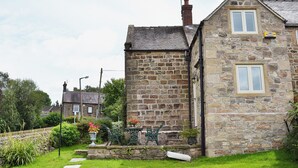 Une maison en pierre avec un toit en pente, un petit jardin agrémenté de pas japonais et un banc.