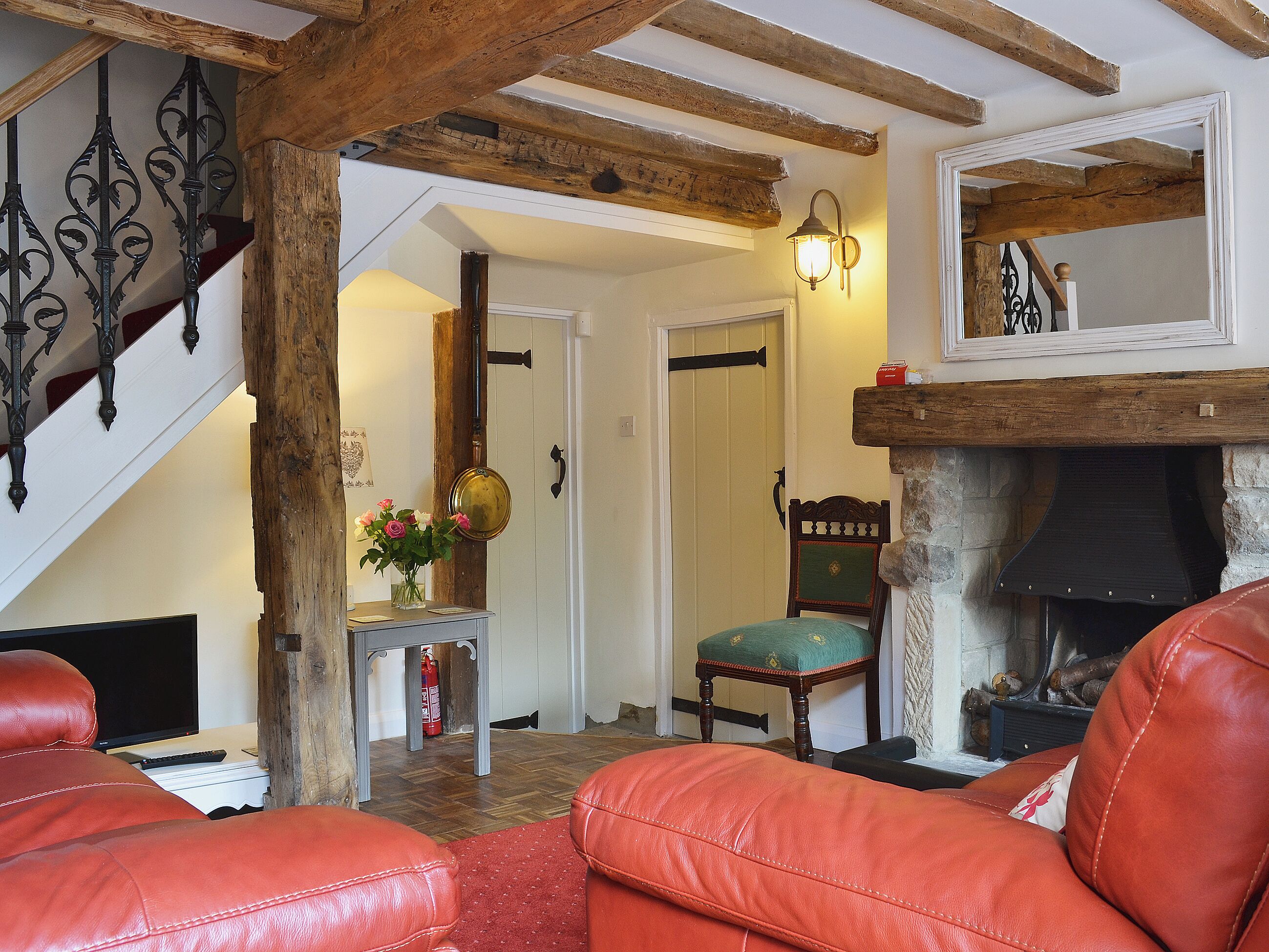 A cozy living room with a fireplace, leather chairs, a wooden staircase, and a small table with a vase of flowers.