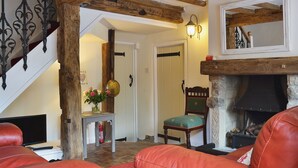 Un salon chaleureux avec une cheminée, des fauteuils en cuir, un escalier en bois et une petite table sur laquelle est posé un vase de fleurs.
