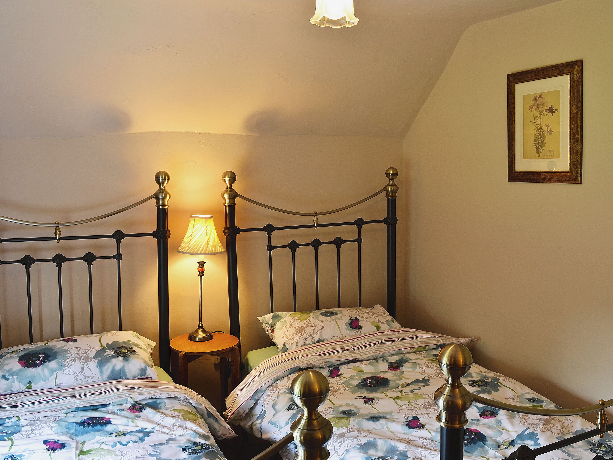 A bedroom with two single beds, a nightstand, a lamp, and a framed picture on the wall.