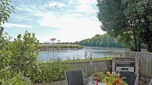 An outdoor patio with a table set for two, overlooking a river. - 4 bedroom accommodation in Warkworth (Warkworth)