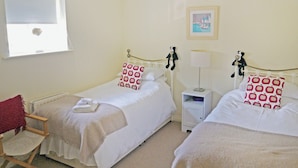 A room with two single beds, a chair, a nightstand with a lamp, and a window. - 4 bedroom accommodation in Warkworth (Warkworth)