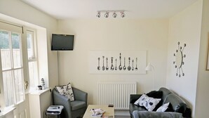 A living room with a grey sofa, a wooden coffee table, a TV, and a wall with a clock and spoon illustrations. - 4 bedroom accommodation in Warkworth (Warkworth)