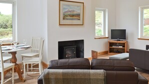 A living room with a fireplace, a television, and a dining area with chairs and a table. - 2 bedroom accommodation in Fasach, near Dunvegan (Fasach, near Dunvegan)