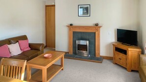 A living room with a fireplace, a sofa, a coffee table, a TV stand, and a dining area. - An attractive luxurious ground floor apartment in the centre of Keswick. (Keswick)