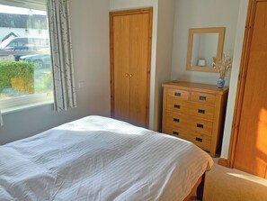 Un dormitorio con cama, armario de madera, cómoda y ventana con vistas al exterior.