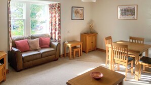 A living room with a sofa, a dining table with chairs, a wooden cabinet, and a lamp. - An attractive luxurious ground floor apartment in the centre of Keswick. (Keswick)
