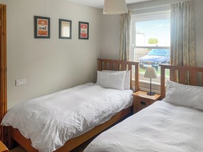 Une chambre avec deux lits simples, une table de chevet avec une lampe et trois tableaux encadrés accrochés au mur.
