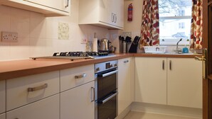 A kitchen with white cabinets, a gas stove, an oven, a window with curtains, and a sink. - An attractive luxurious ground floor apartment in the centre of Keswick. (Keswick)